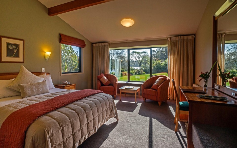 Spacious guest room at Wilderness Lodge Arthur’s Pass with garden views, warm lighting and natural décor.